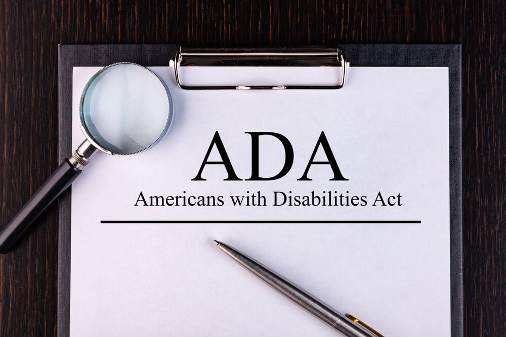 ADA compliance_Text ADA Act. is written on a notebook with a pen and a magnifying glass lying on the table. Business concept.