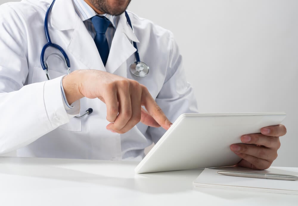 ppc doctors_Close up of male therapist hands using tablet computer. Physician in white medical uniform with stethoscope sitting at desk. Modern technology in examination and diagnosis. Medical digital application