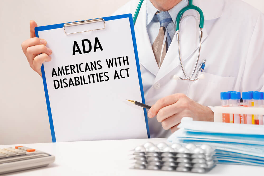 ADA compliance_Doctor holds paper with American Disabilities ADA, stethoscope and pills on table