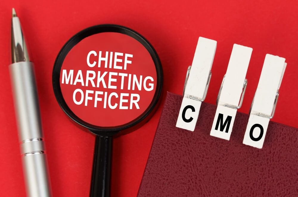 CMO_Business concept. On the red surface lies a pen, a notebook with clothespins - CMO, and a magnifying glass with the inscription - Chief Marketing Officer