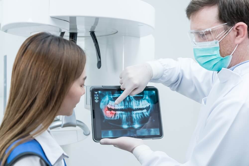 dental website_Caucasian male dentist hold digital tablet and explaining tooth problem. Caucasian male doctor use tablet and giving advice or consultation to Asian young girl patient about oral care in dental clinic