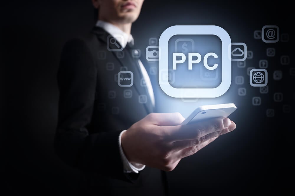 PPC_businessman holding a mobile phone with applications icons and ppc text on virtual screen. Internet concept. business concept
