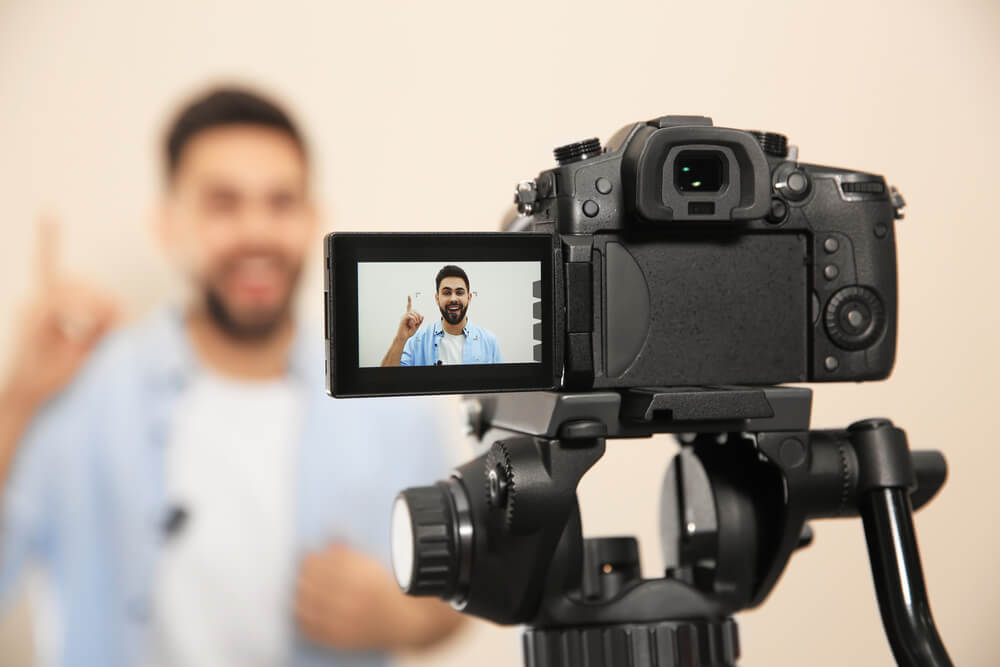 video marketing_Young blogger shooting video with camera against beige background, focus on screen