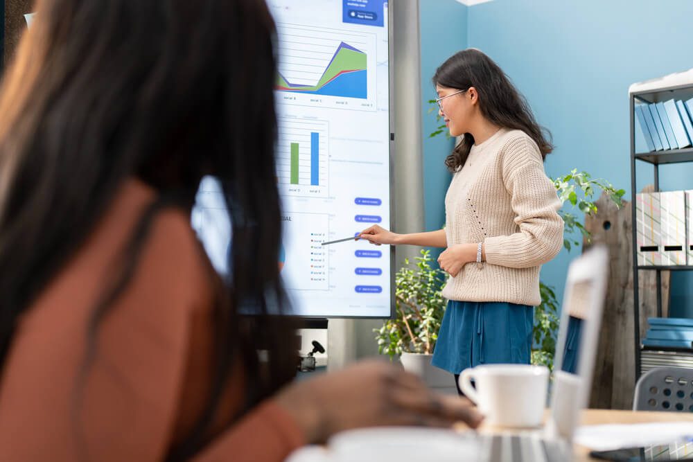 ecommerce ranking_Marketing graduate intern leads first business meeting, explains company's sales rankings and charts. The girl is facing the interactive whiteboard, she is stressed about speaking in front of workmate