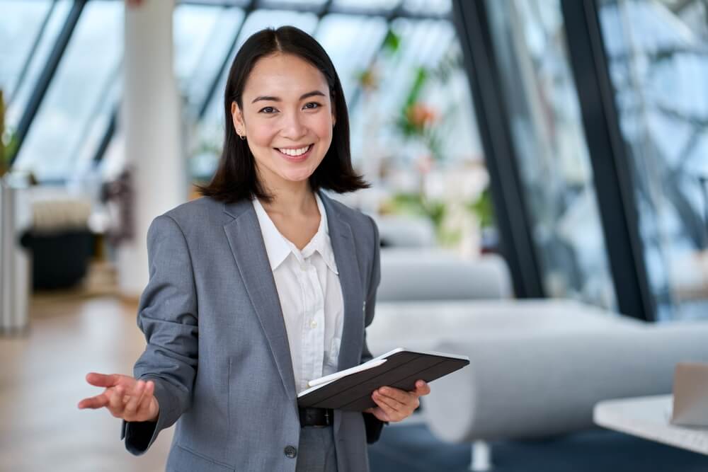 marketing consultant_Happy young Asian saleswoman looking at camera welcoming client. Smiling woman executive manager, secretary offering professional business services holding digital tablet standing in office. Portrait