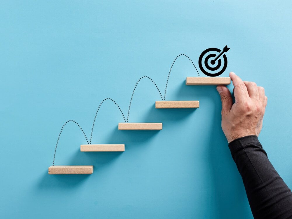 goals_Male hand arranges a wooden block staircase with target icon. Achieving goals and objectives or goal setting concept.