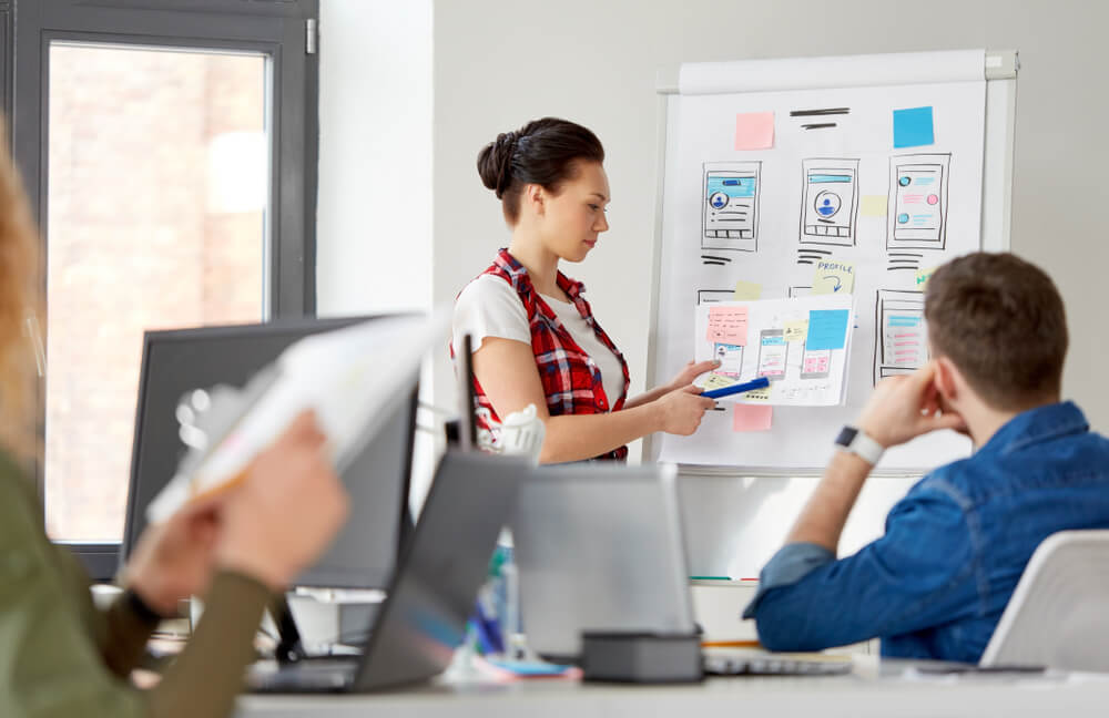 UX_business, technology and people concept - woman showing user interface design on flip chart to creative team at office presentation