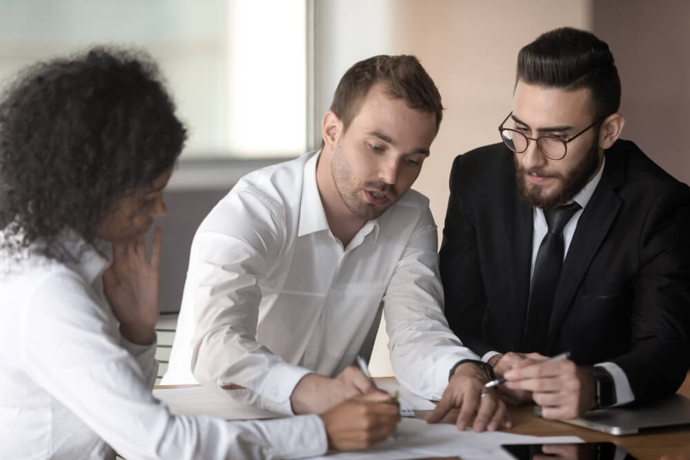 CMO_European team leader lead corporate meeting seated at desk with arabian and african ethnicity diverse teammates businesspeople working together strategizing reviewing document analyzing financial data