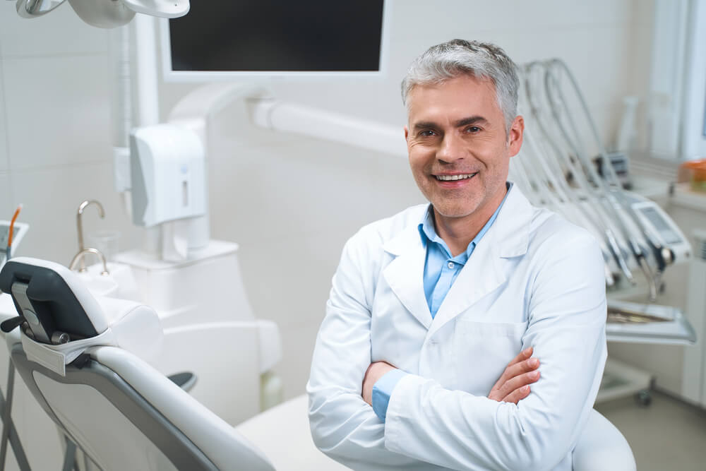 dentist_Smiling man in medical uniform is sitting in clinic near equipment and waiting for patient. Website banner