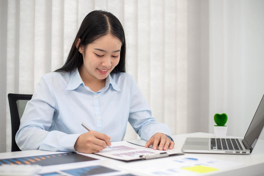 CMO_Portrait of businesswoman with laptop writes on a document and check graph at her office