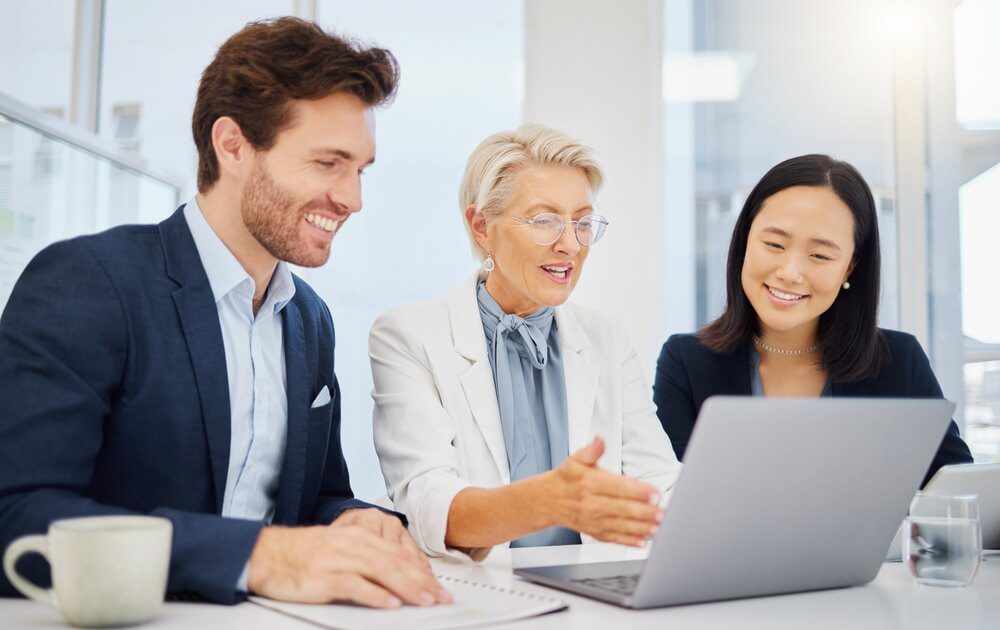 revenue team_Laptop, happy and business people reading online research article, positive progress report or company innovation plan. Workplace, strategy success and diversity staff happiness for revenue growth