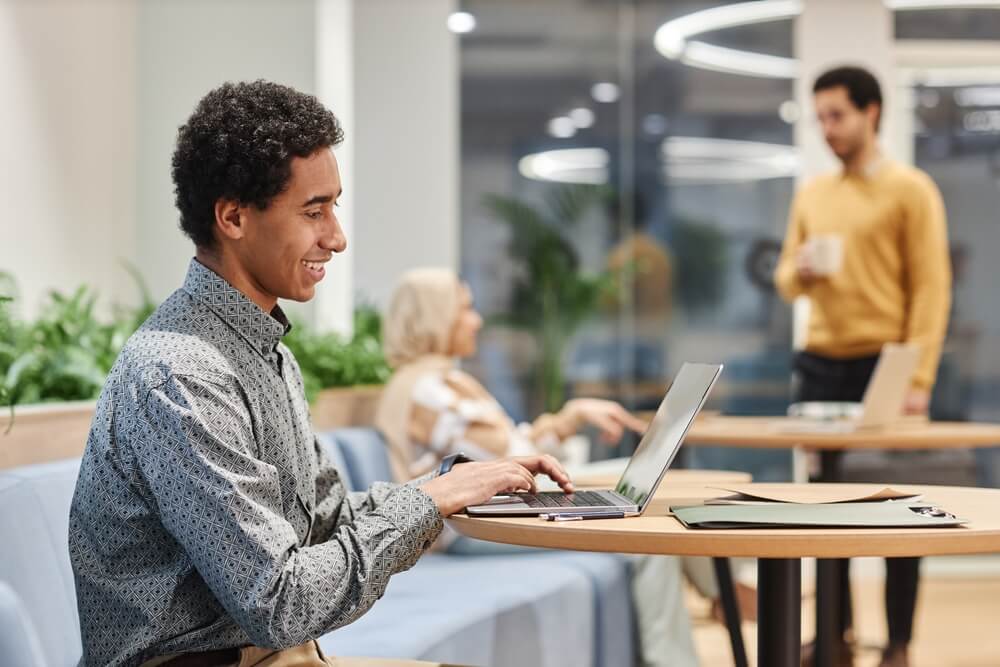 seo services_Side view portrait of smiling Middle Eastern man working with laptop in creative office space, copy space