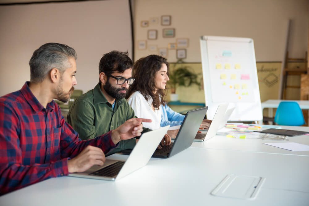 UX design_Business team training to use new corporate software, using laptops at conference table. Business colleagues in casual working together in contemporary office space. Corporate meeting concept