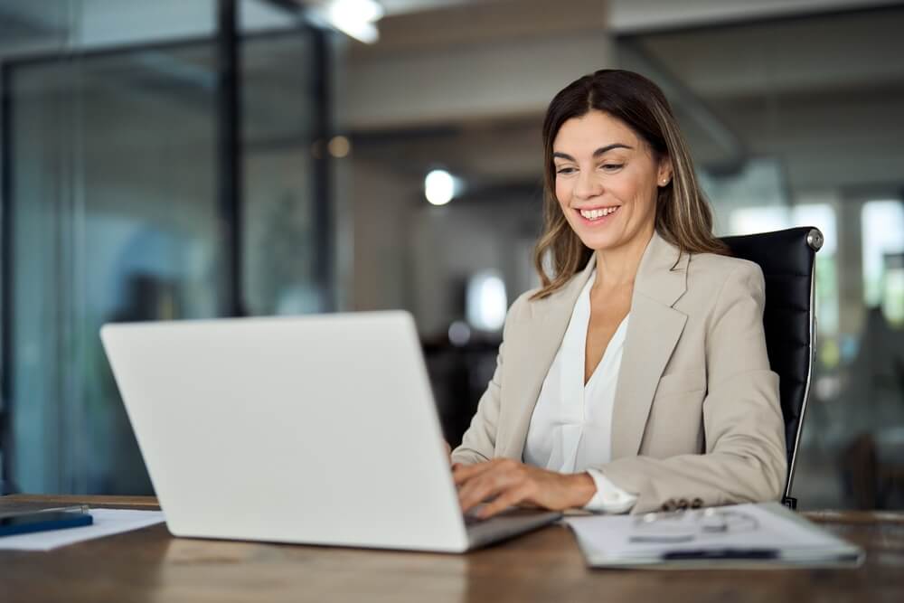 SEO_Happy mature business woman entrepreneur in office using laptop at work, smiling professional middle aged 40 years old female company executive wearing suit working on computer at workplace.