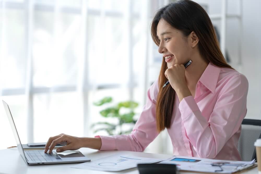 FCMO_Beautiful asian businesswoman working on laptop and calculating with financial calculator from statistics data graphs, charts. Successful business results in modern office with joy.