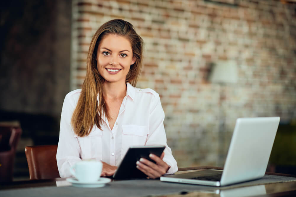 CMO_Businesswoman using tablet while sitting in cafeteria. On table laptop and coffee.