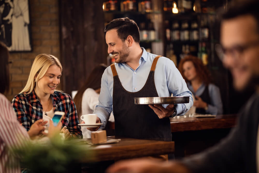 ethnic restaurant_Young happy woman enjoying while waiter is serving her coffee in a cafe.