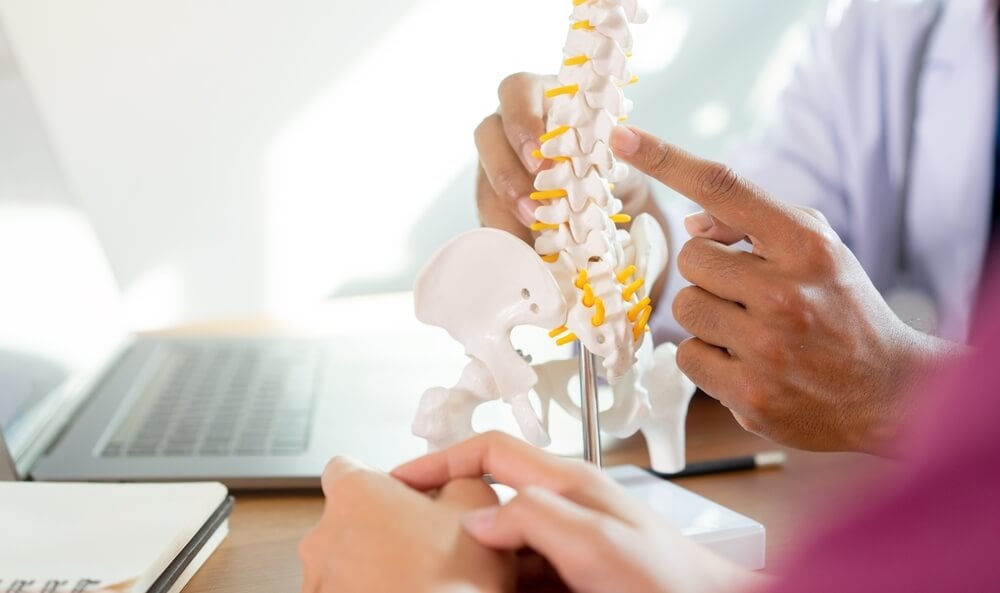 chiropractor_close up physical therapist hand pointing on human skeleton at low back to advise and consult to patient to treatment at office for healthcare concept