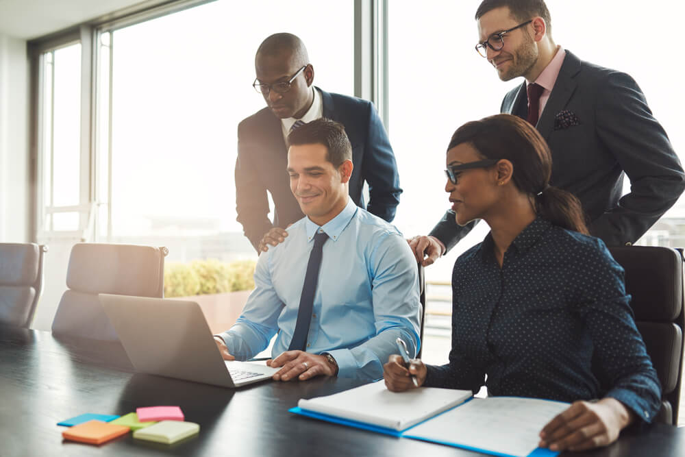B2B_Group of happy diverse male and female business people in formal gathered around laptop computer in bright office