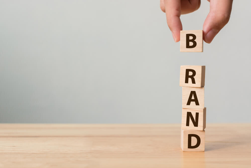 brand_Hand of male putting wood cube block with word BRAND on wooden table. Brand building for success concept