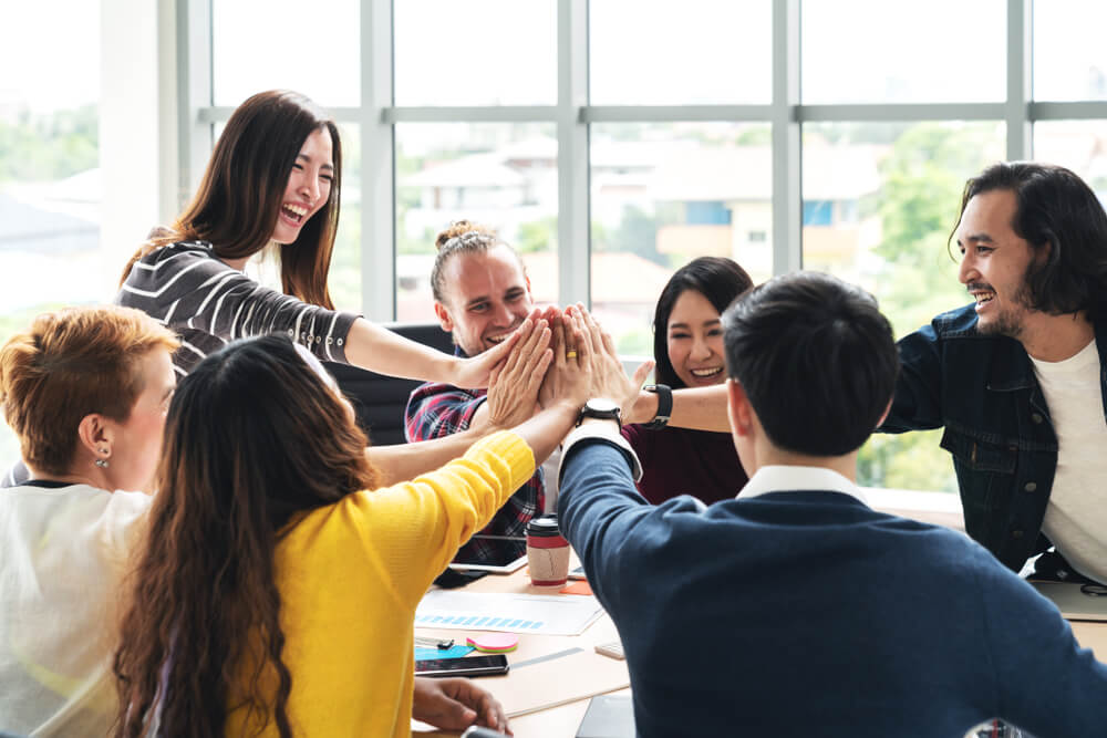 employee engagement_group of young multiethnic diverse people gesture hand high five, laughing and smiling together in brainstorm meeting at office. Casual business with startup teamwork community celebration concept.