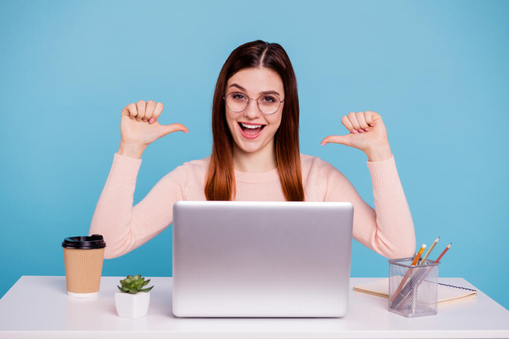 brand_Close up photo beautiful she her foxy lady hands arms fingers indicate direct herself advertising notebook coffee cup table desk wear specs casual pastel warm pullover isolated bright blue background