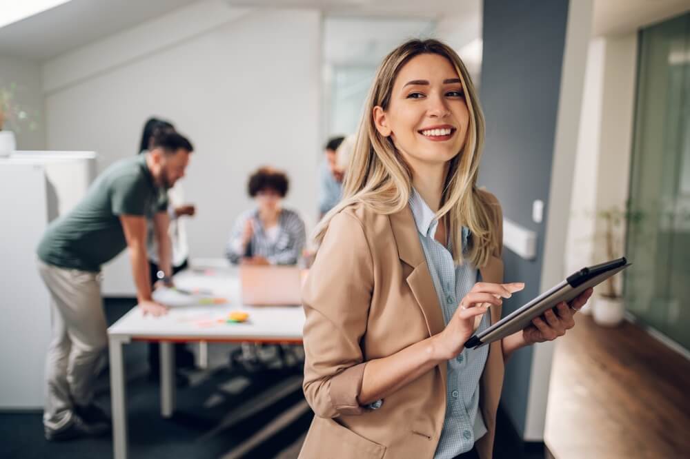 startup business_Smiling confident business leader looking at camera and standing in an office at team meeting. Portrait of confident businesswoman with colleagues in boardroom. Using digital tablet during a meeting.