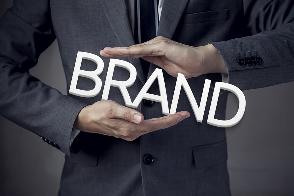 brand_Businessman in suit with two hands in position to protect the word "BRAND" (focus on hand, blur out the suit).