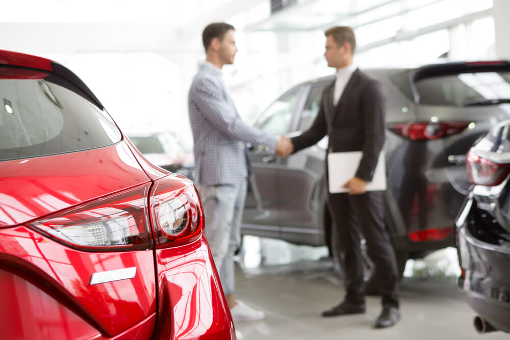 car dealership_Selective focus on a new car at the dealership professional salesman and his client shaking hands on the background copyspace professionalism agreement contract leasing renting retail sales.