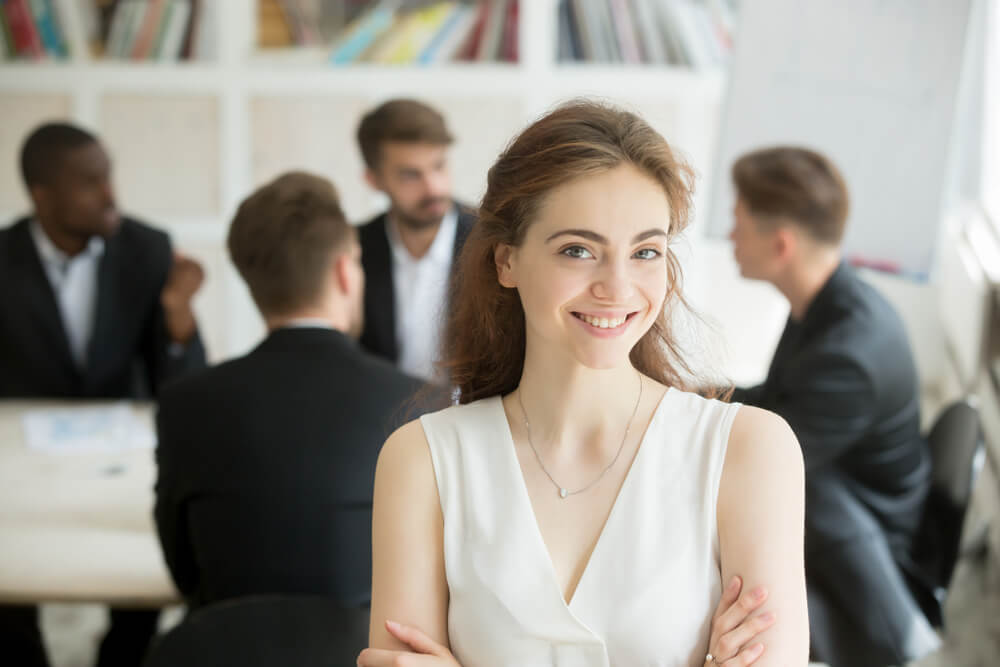 CMO_Attractive female leader standing with arms crossed in front of male executive team meeting, smiling businesswoman looking at camera, friendly woman boss, assistant or hr manager headshot portrait