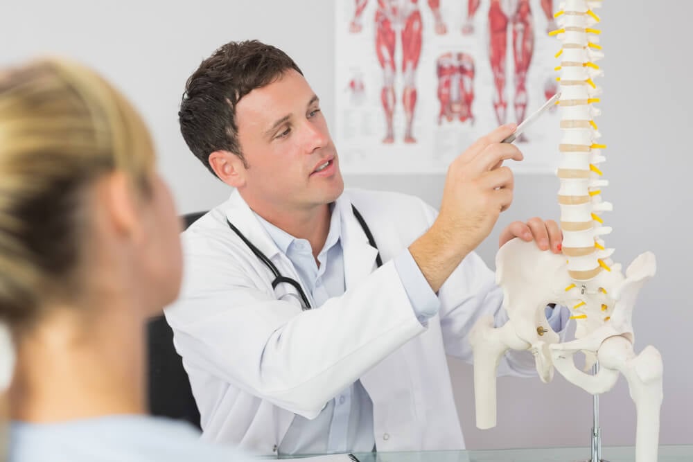 chiropractors_Good looking doctor showing a patient something on skeleton model in bright office