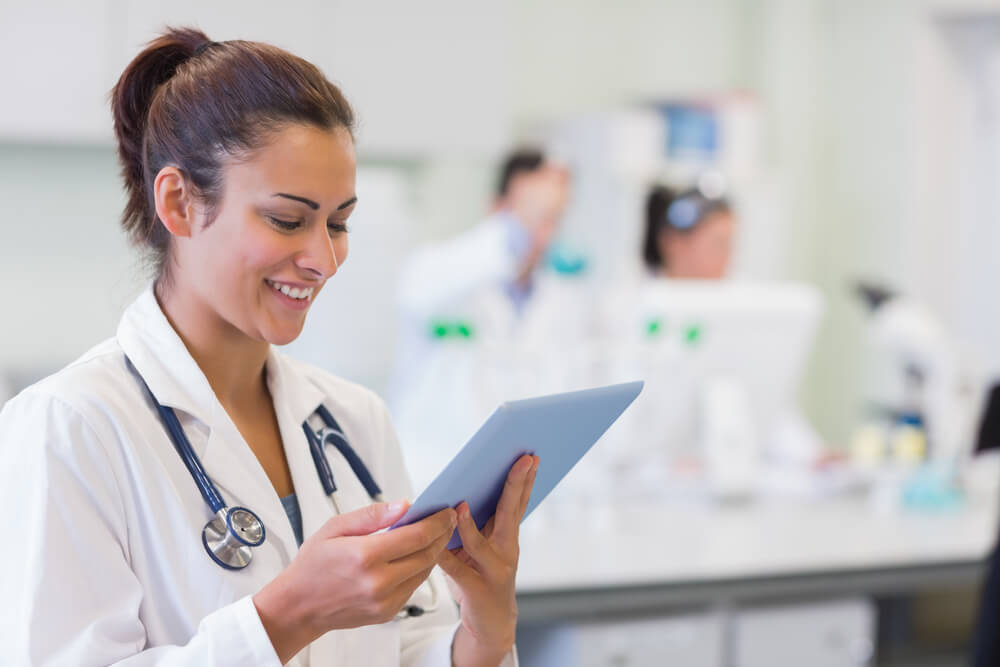 healthcare content marketing_Close-up of a female doctor using tablet PC with colleagues in background at medical office