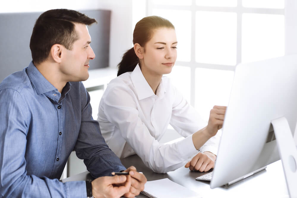 CMO_Cheerful smiling businessman and woman working with computer in modern office. Headshot at meeting or workplace. Teamwork, partnership and business concept