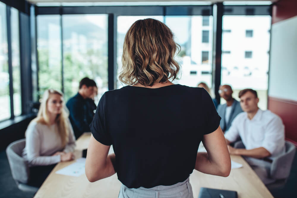 marketing leadership_Rear view of a businesswoman addressing a meeting in office. Female manager having a meeting with her office staff.