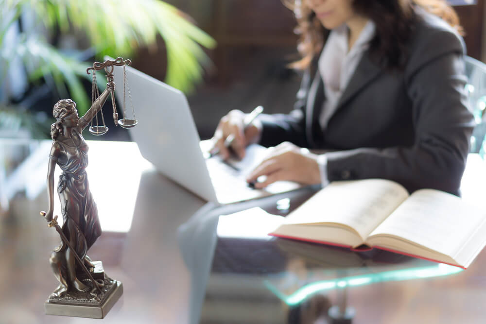 lawyers_Lawyer office. Statue of Justice with scales and lawyer working on a laptop. Legal law, advice and justice concept.