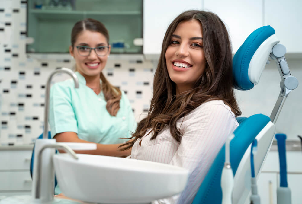 dentist_Gorgeous young woman with perfect smile siting in dentist chair and looking at camera, dentist in background. focus on patient