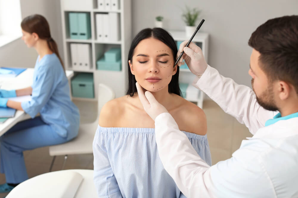 plastic surgeon_Plastic surgeon applying marks on patient's face in clinic