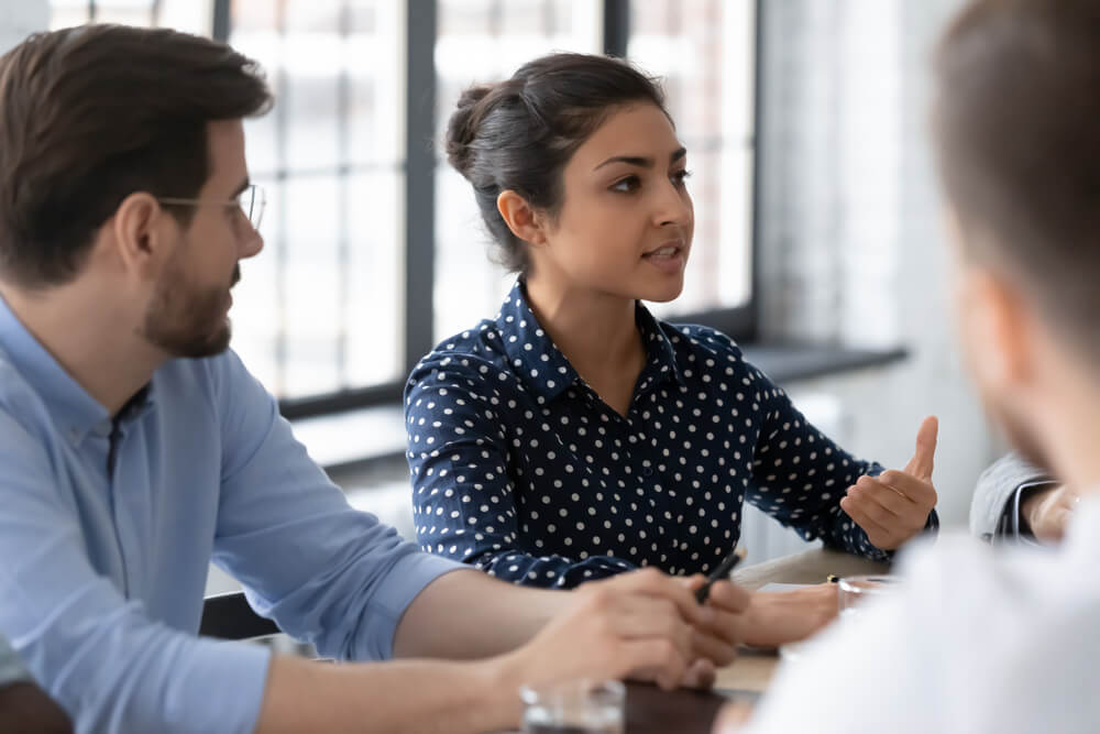 marketing strategy_Point of view. Young biracial female employee talking to colleagues at workshop sharing her vision of problem solution, indian lady manager introducing product service to clients on business meeting