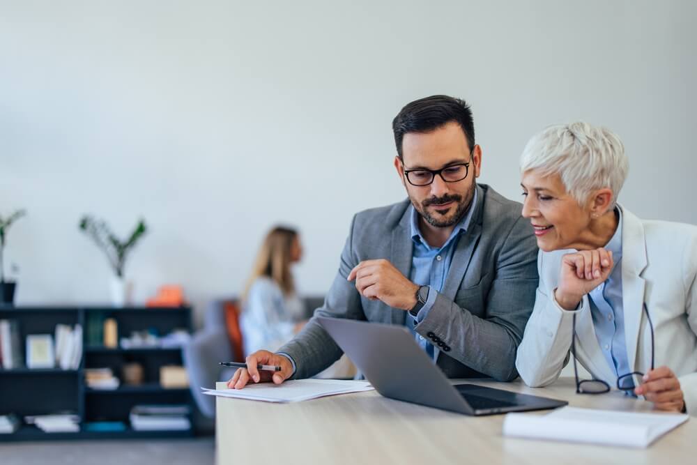 SEO_An adult man and mature woman working at the office together, using a laptop.