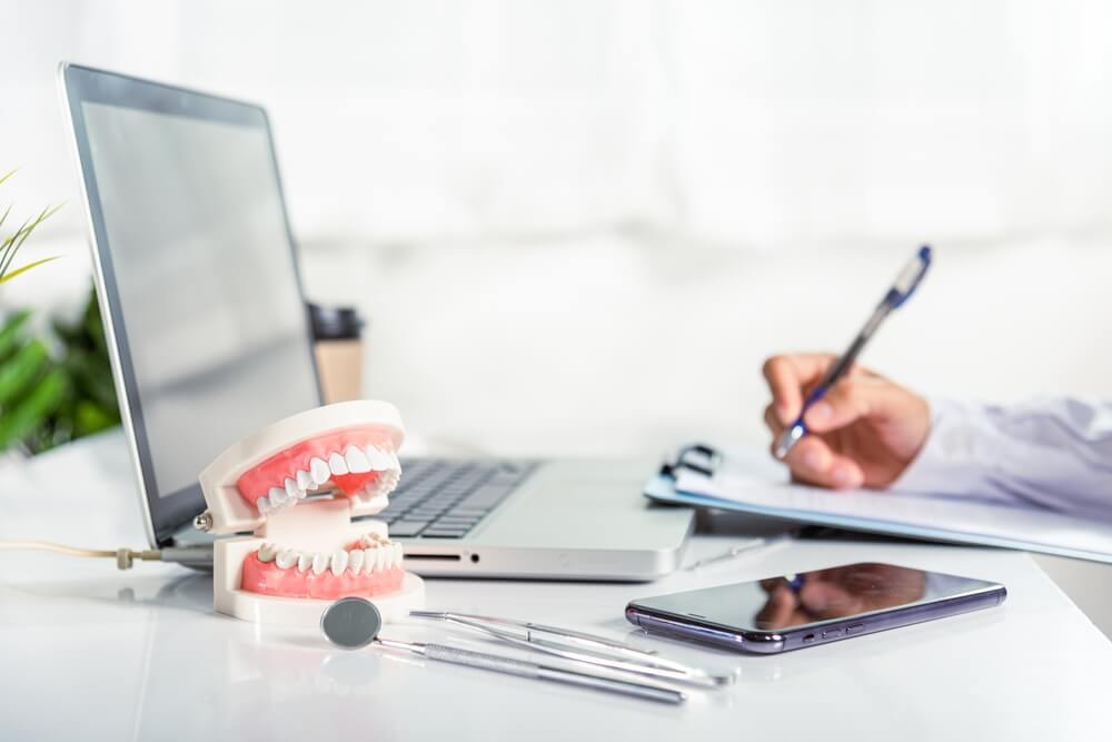 dentist_Oral dental. Dentist doctor in uniform writing information of patient in paperwork checklist on clipboard on desk office, teeth model, X-ray on laptop screen, prescription medical dental healthcare