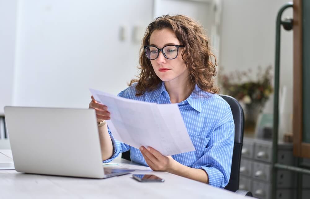 accounting_Young busy business woman manager, lawyer or company employee holding accounting bookkeeping documents checking financial data or marketing report working in office with laptop. Paperwork management