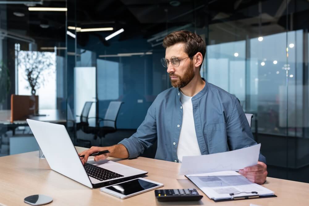 accounting_Serious and focused financier accountant on paper work inside office, mature man using calculator and laptop for calculating reports and summarizing accounts, businessman at work in casual clothes.