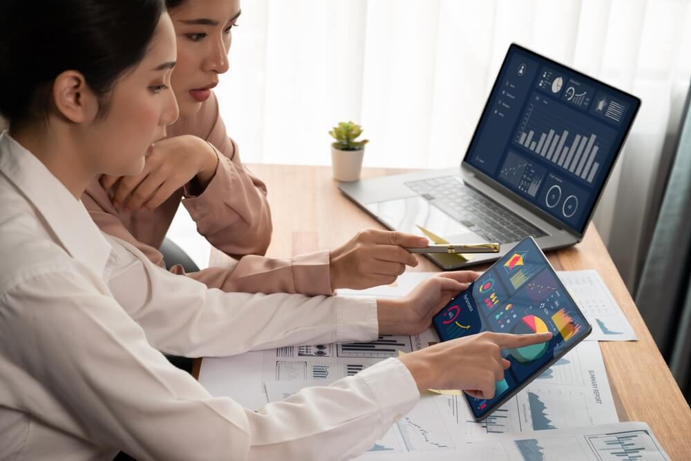 data analytics_Analyst team colleague discuss financial data on digital dashboard, analyzing charts graph display on laptop and tablet screen. Modern office use business intelligence to plan marketing. Enthusiastic