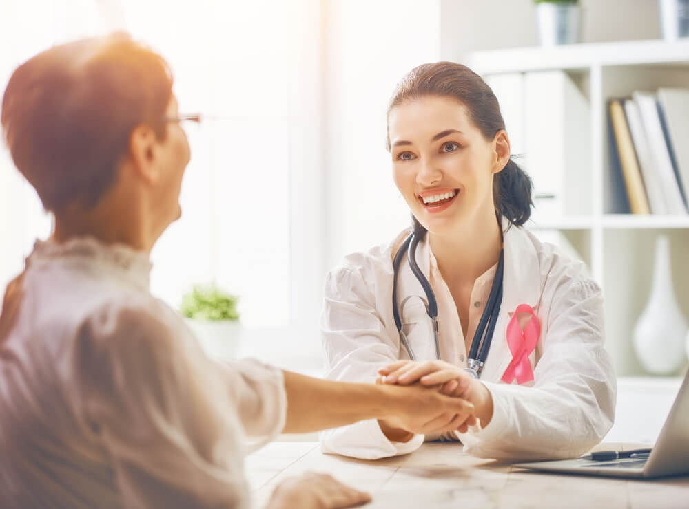 doctor ppc_Pink ribbon for breast cancer awareness. Female patient listening to doctor in medical office. Raising knowledge on people living with tumor illness.