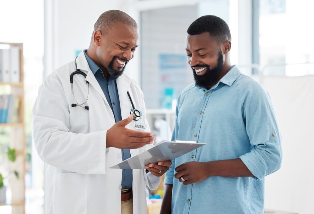 healthcare_Healthcare, black man and doctor with clipboard, diagnosis and conversation for results, smile and care. Male patient, guy and medical professional with documents, paperwork for insurance and talking