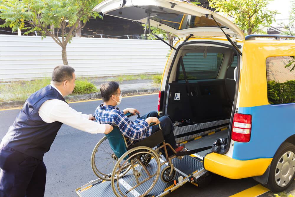 medical transport_driver helping man on wheelchair getting into taxi