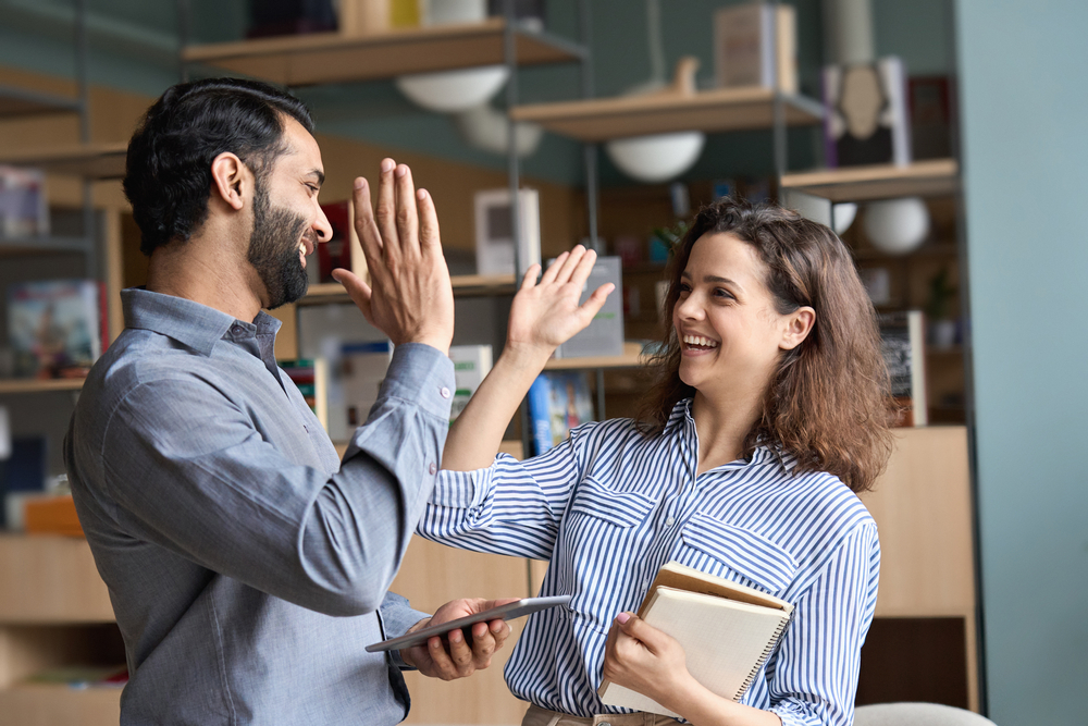 wo happy friendly diverse professionals, teacher and student giving high five standing in office celebrating success, good cooperation result, partnership teamwork and team motivation in office work.