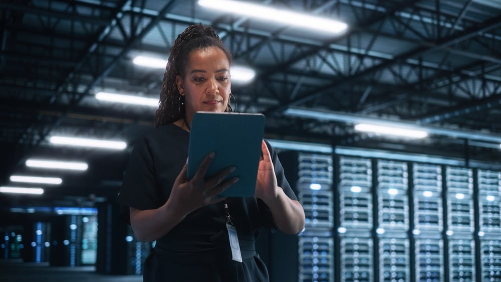 Connect With SaaS Industry Influencers Via a Fractional CMO: Here's How 1 Successful Female IT Specialist Using Laptop Computer, while Standing at Big Warehouse Data Center. System Administrator working with Computing SAAS, Cloud Services.