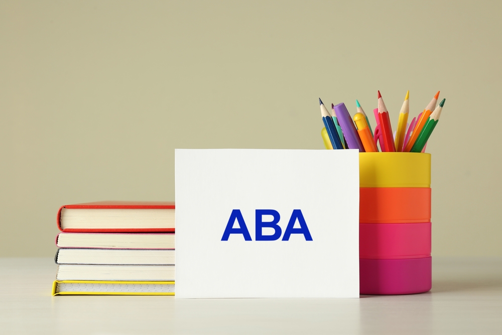 Set of stationery and card with abbreviation ABA (Applied Behavior Analysis) on wooden table against beige background