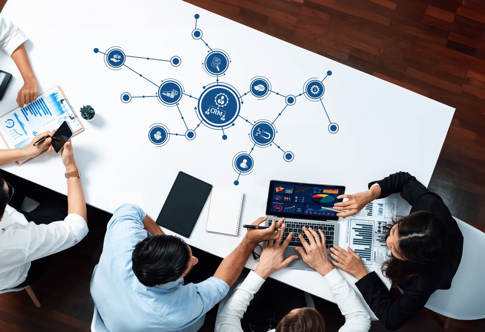 A diverse team collaborates in a modern office setting, analyzing data and discussing business strategies with a laptop and documents focused on CRM insights and visualizations